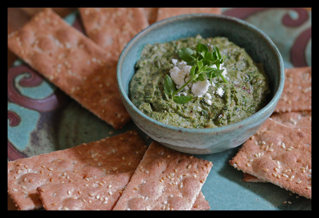 A bowl of Pecan Feta Wild Greens Pesto surrounded by crackers.