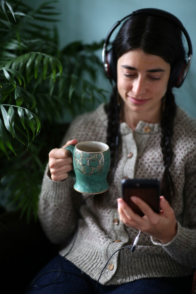 A person wearing headphones and holding a mug.