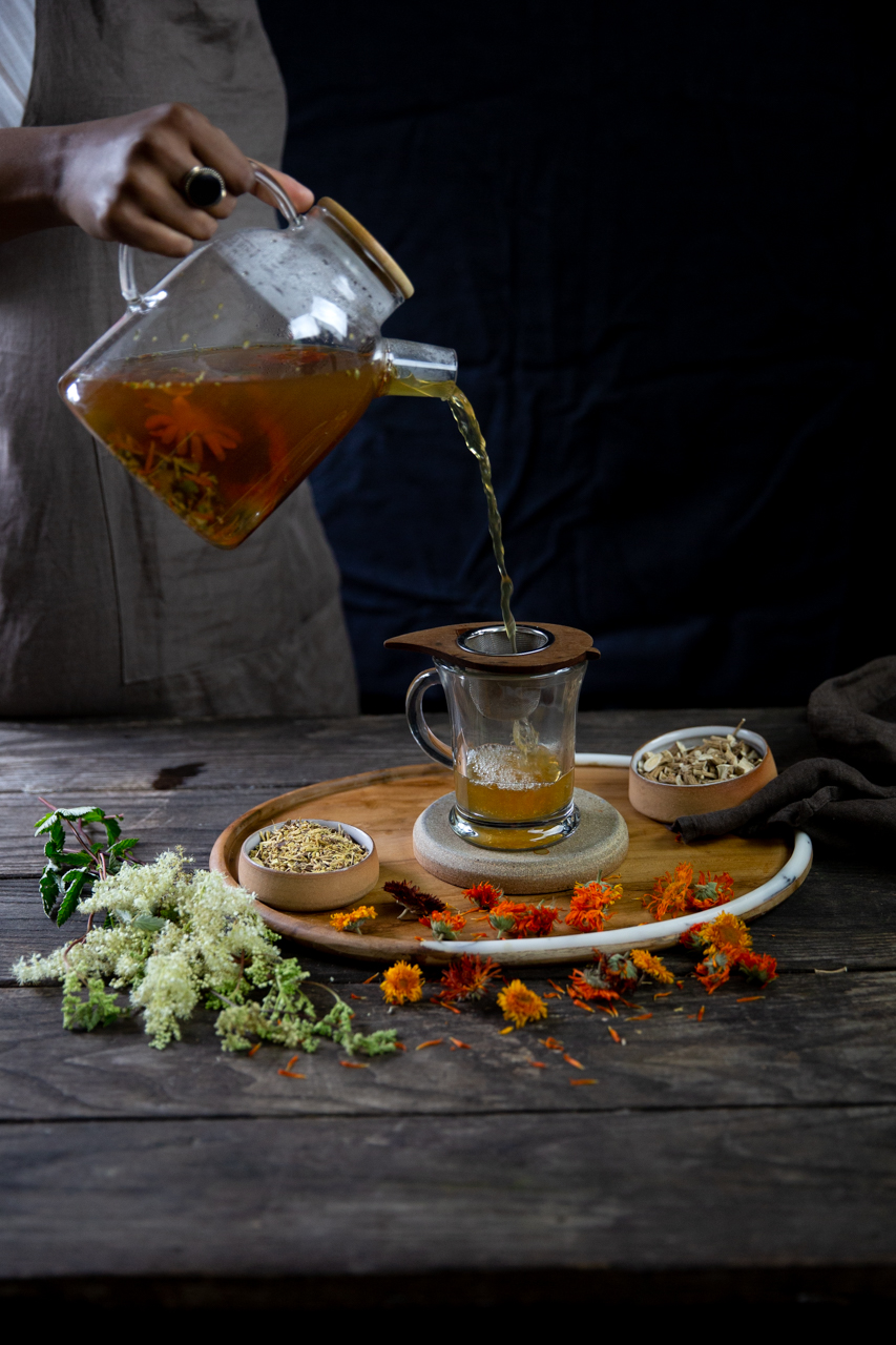 A person pours a cup of calendula tea through a strainer.