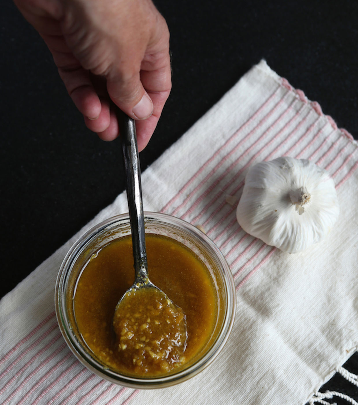 Hand holding spoon dipped in medicinal garlic sauce.