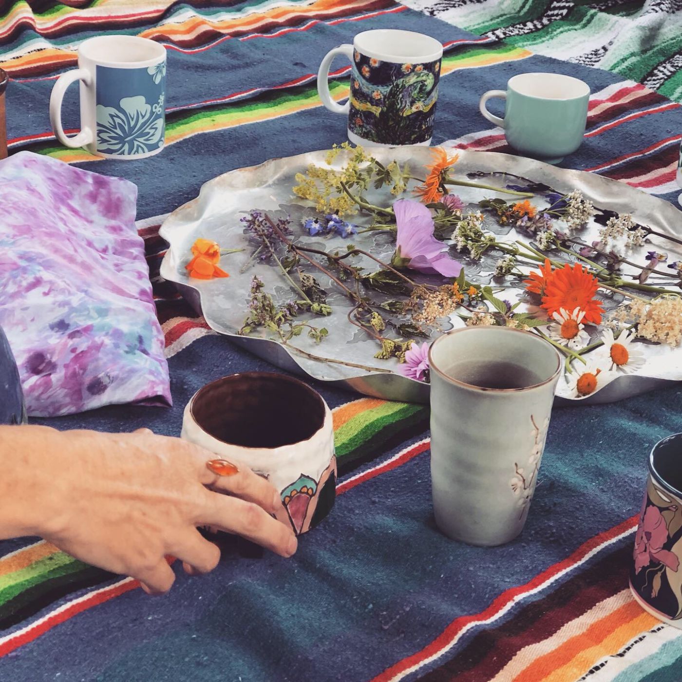 A woman's hand touches a mug near a tray of herbs.