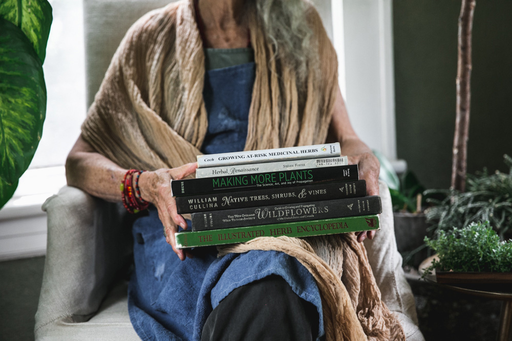 A person seated while holding a stack of herbalism books.
