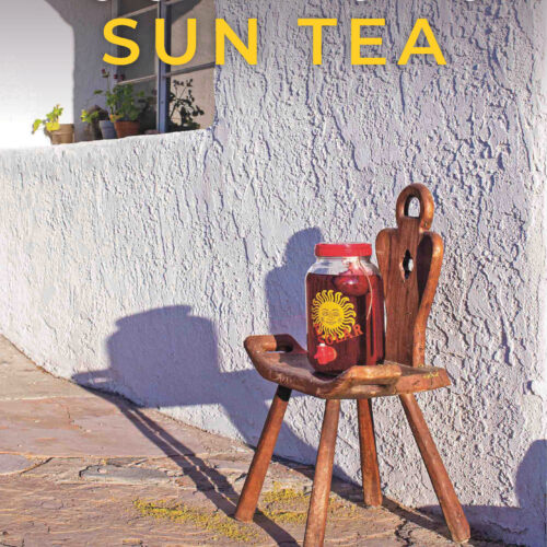 A large jar of Isis Hibiscus Sun Tea sits on a wooden chair outside a stucco building.