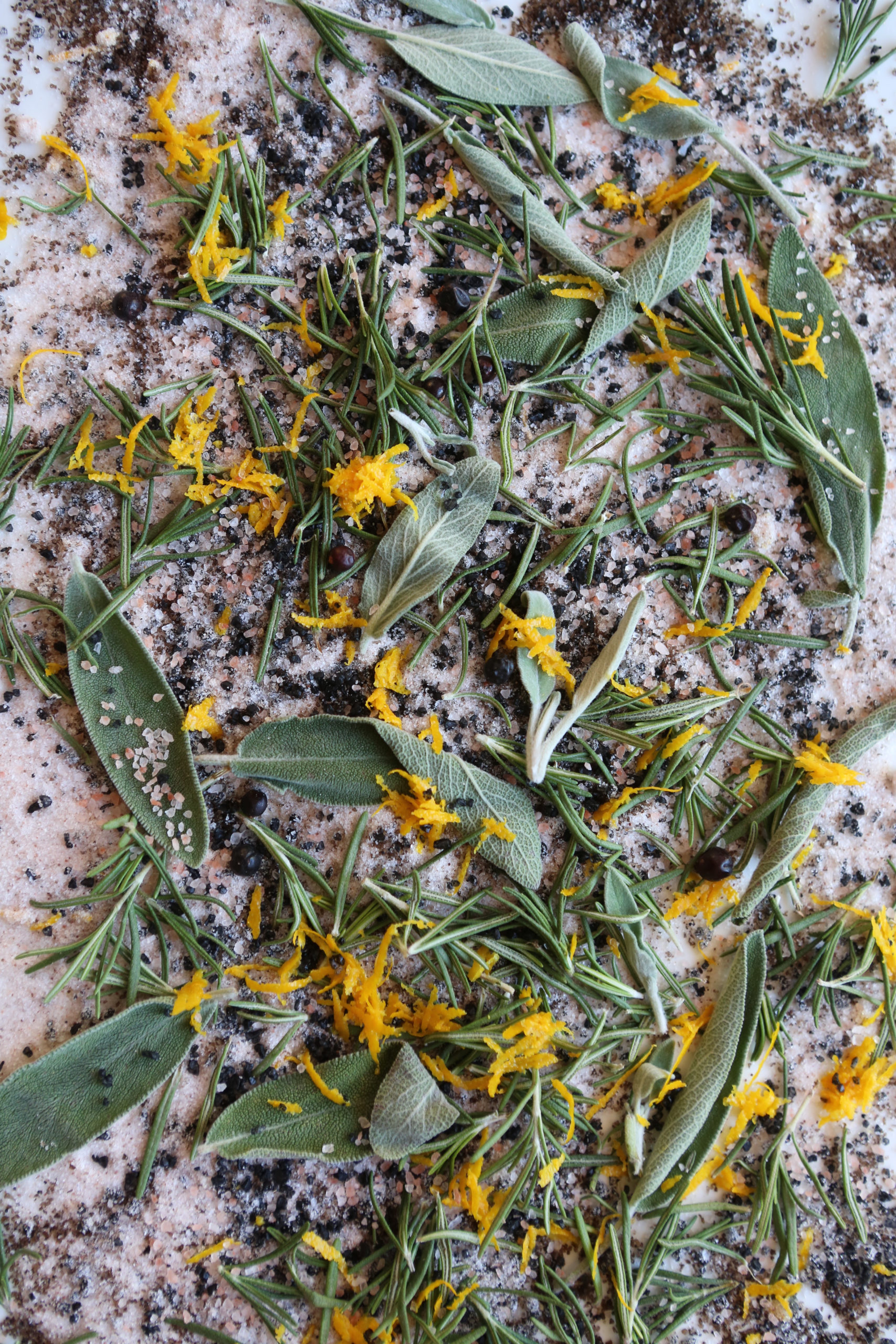 A close up of herbal finishing salt made from fresh sage, rosemary, orange zest, and juniper berries.