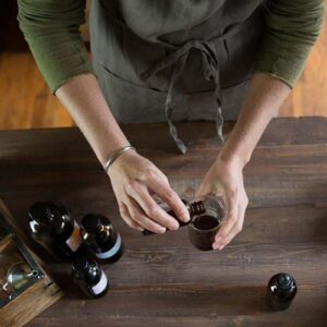 Two hands over a wooden table, pouring a herbal tincture into a beaker.