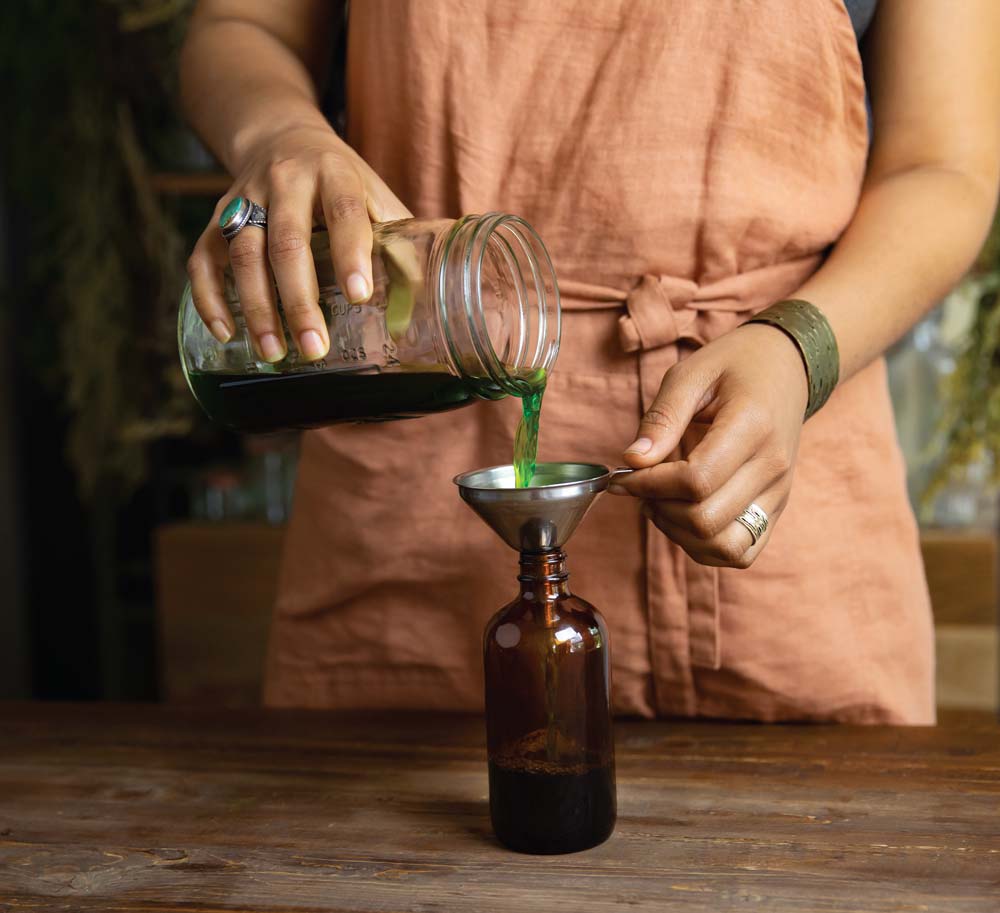 A person pours freshly made herbal tincture into an amber glass bottle.